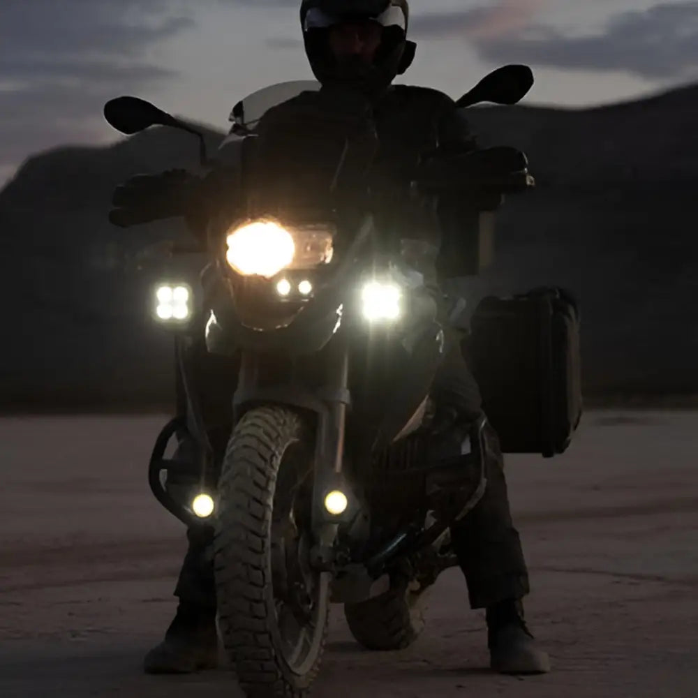 Motorcycle with illuminated headlights at night, featuring Denali Ekstralys Brakett for BMW R1300GS